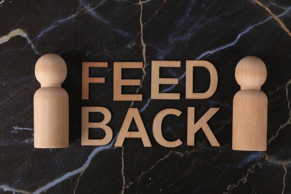 Wooden letters spelling 'Feedback' with peg-like figures on marble background.