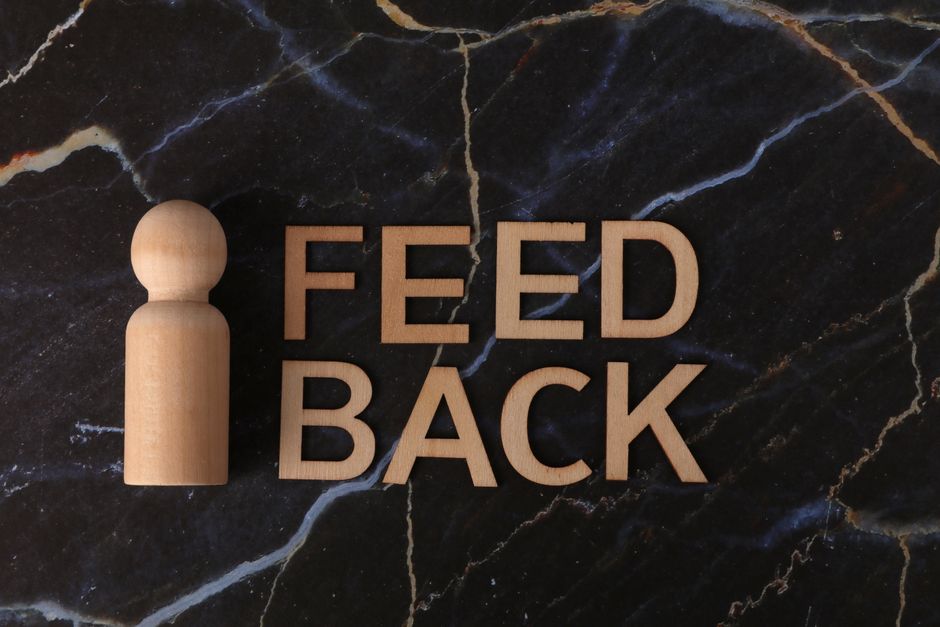 Wooden letters spelling 'FEEDBACK' on a dark marble surface with a wooden figure.