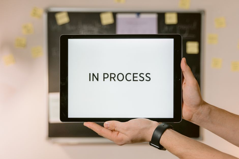 Close-up of hands holding a tablet displaying 'In Process' text, emphasizing workflow.